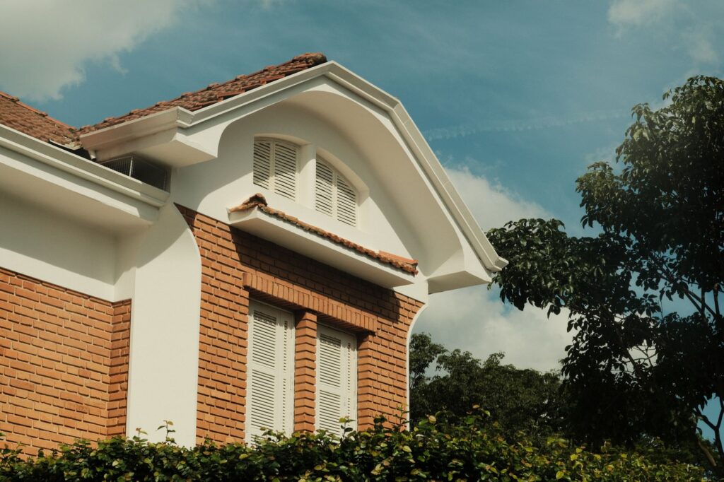Exterior shot of a brick house featuring an arched roof and white shutters, set against a blue sky.