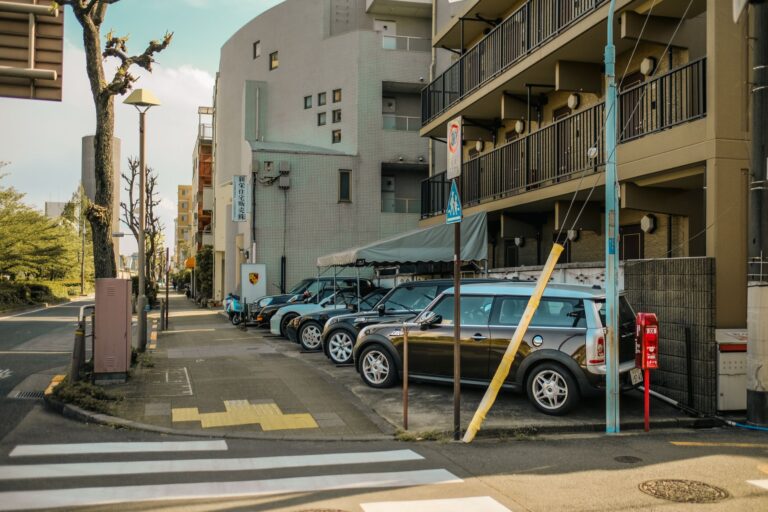 A street view capturing parked cars alongside residential buildings on a sunlit day.