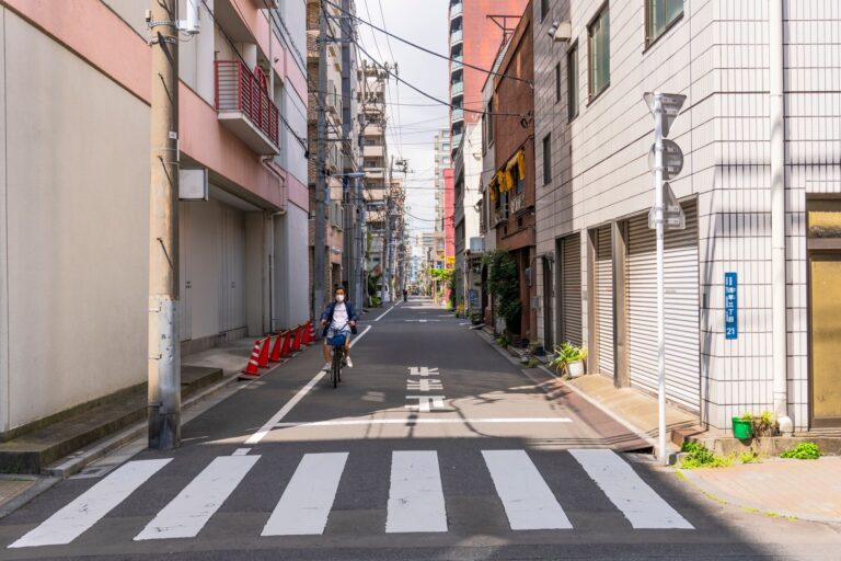 A cyclist rides along a quiet urban street in Japan, showcasing typical residential architecture.