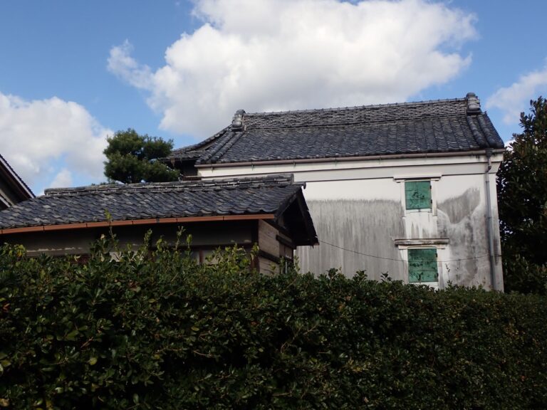 Vintage Japanese house with grey tile roof, set against clear skies, offering cultural charm.