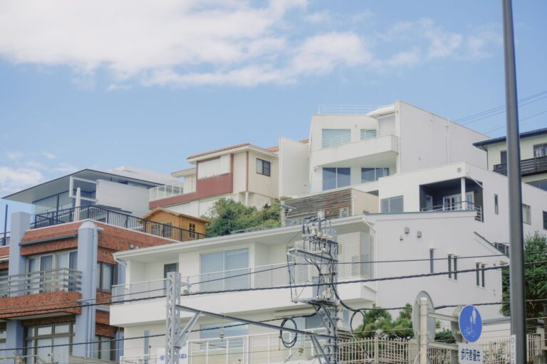 Contemporary houses on a hillside in a Japanese coastal town, under a blue sky.