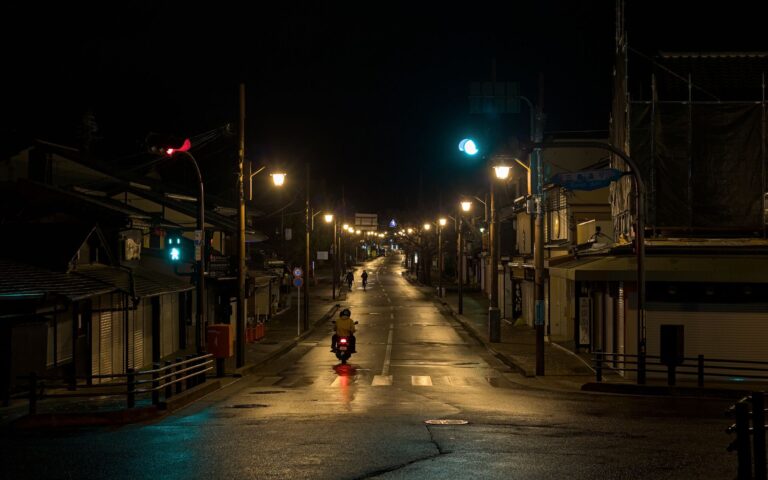 A tranquil night scene in Arashiyama, Kyoto, with streetlights and a lone motorbike.