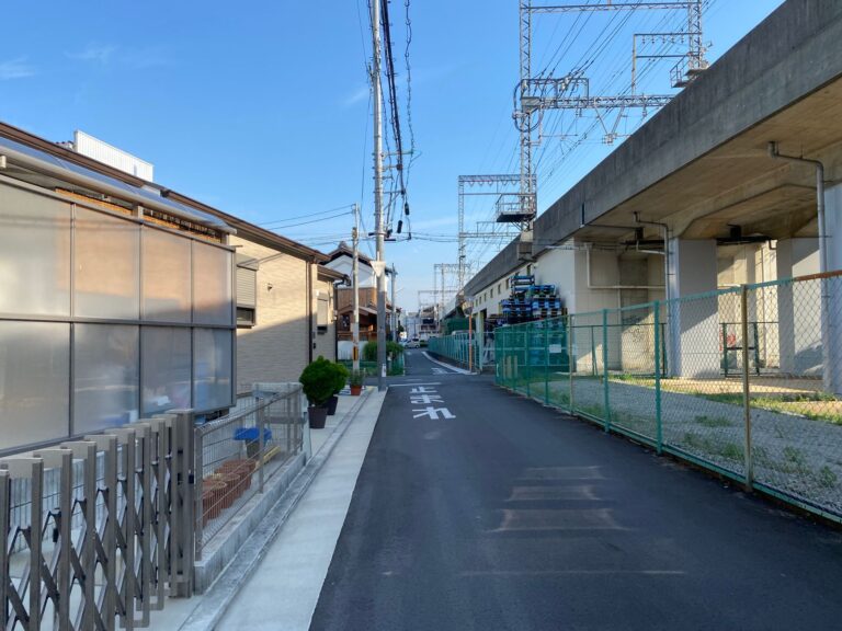 Quiet residential street in Osaka, Japan, featuring overhead train tracks and minimal traffic.
