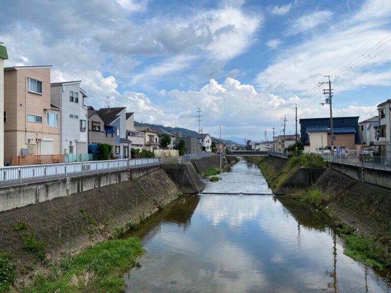 Charming urban canal reflecting houses and clouds under a clear sky.