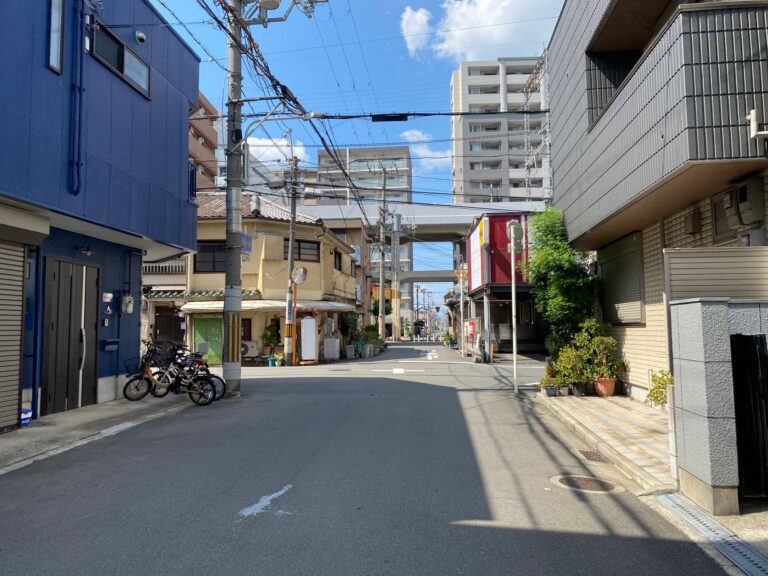 Quiet urban street scene with residential buildings under a clear blue sky and overhead power lines.