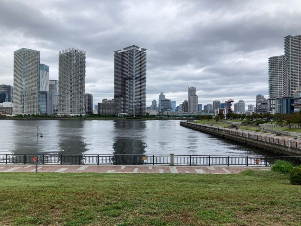 Scenic view of Tokyo skyline from Odaiba, featuring modern skyscrapers and waterfront promenade under cloudy skies.