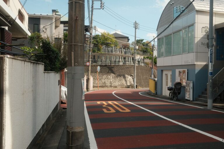 A quiet street in Shinjuku City, Tokyo, showcasing curved road design and urban architecture on a sunny day.
